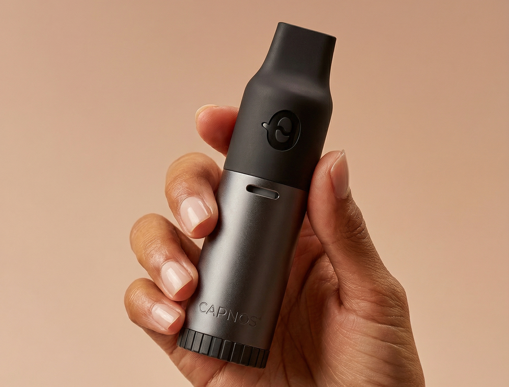 Hand holding a black and silver device with 'CAPNOS' quit vaping device